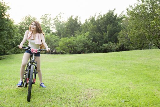 Woman riding an exercise bike in the park. On the lawn in the evening.