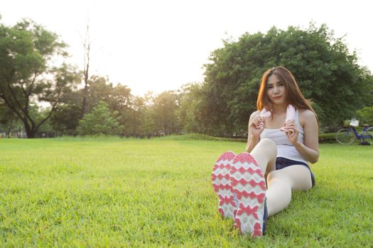 Woman Sitting after jogging. on grass in the park. In the evening