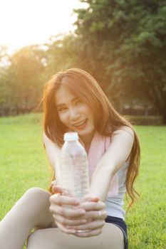 Woman holding a bottle of water and handed it to. Sitting on the lawn after jogging.