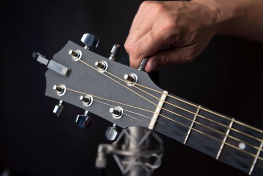 Close-up of a hand turning a guitars tuning pegs with a studio microphone in the background.