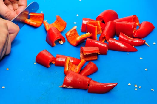 cutting red pepper with knife on blue board
