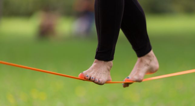 Lady practising slack line in the city park. Slacklining is a practice in balance that typically uses nylon or polyester webbing tensioned between two anchor points.