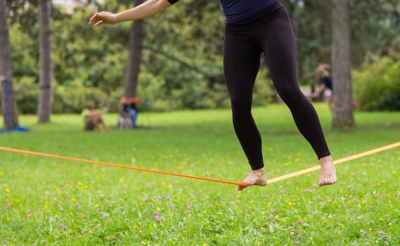 Lady practising slack line in the city park. Slacklining is a practice in balance that typically uses nylon or polyester webbing tensioned between two anchor points.