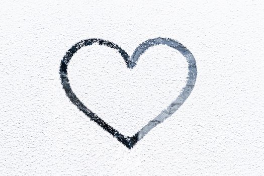 Heart drawn on a glass covered with fresh Christmas snow.