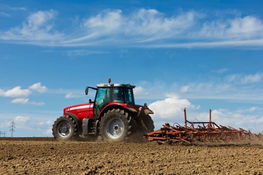 Farmer plowing the field. Cultivating tractor in the field. Red farm tractor with a plow in a farm field. Tractor and Plow