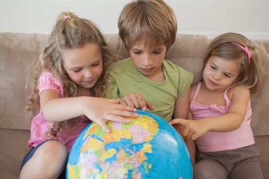 Three young kids with globe sitting in the living room at home