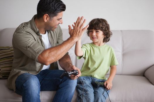 Cheerful father and son playing video games in the living room at home
