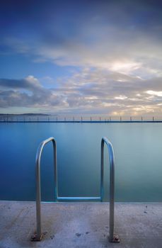 The public ocean rock  pool at Collaroy beach.  Vertical crop.   Collaroy Rock Pool has two odd-shaped classic ocean baths with chains, including a 50-metre lap pool.    Long exposure.  Note ocean pool, not a private or commercial pool. 