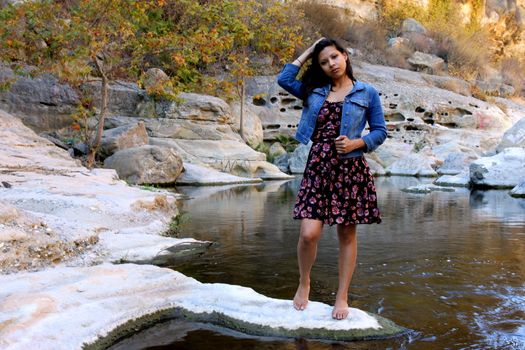 Young Hispanic woman near a creek with a dress and a blue jacket.