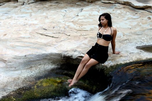 Hispanic woman with bikini lying next to a waterfall.