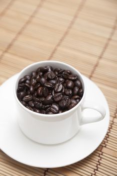 Roasted coffee beans In white coffee cup on wood.