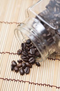 Coffee beans spilled from glass bottle on a wooden table top.