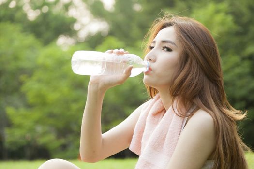 Woman sit and drink after exercise. On the lawn after a workout in the park.