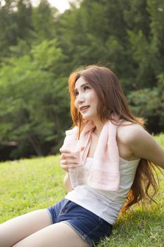 Woman sitting rest after exercise. Hand holding a bottle of water and sit On the lawn.