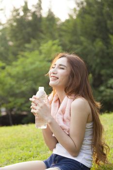 Woman sitting rest after exercise. Hand holding a bottle of water and sit On the lawn.