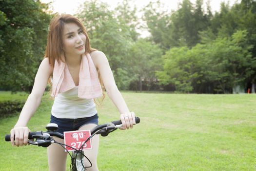 Woman riding an exercise bike in the park. On the lawn in the evening.