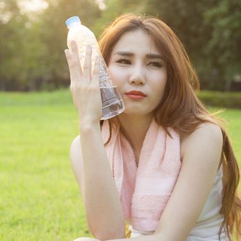 Woman Sitting and holding a bottle of water. Sitting on grass in the park after jogging. In the evening