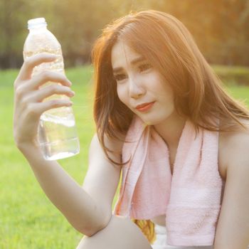 Woman Sitting and holding a bottle of water. Sitting on grass in the park after jogging. In the evening