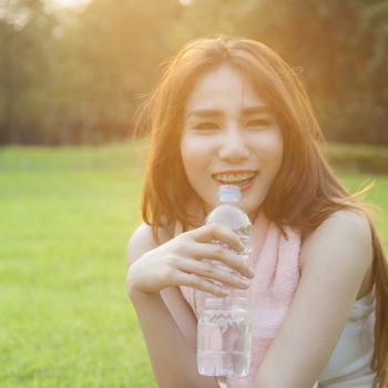 Woman drinking water and sit on grass. After jogging in the evening.