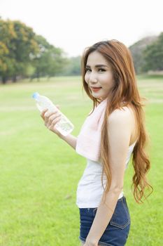 Woman holding a bottle of water. Jogging on grass in the park.