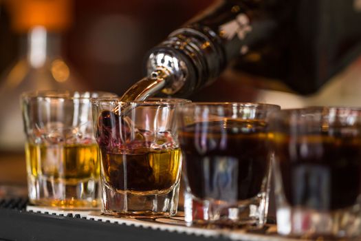 Barman make alcoholic shots with whisky and liqquor in nightclub