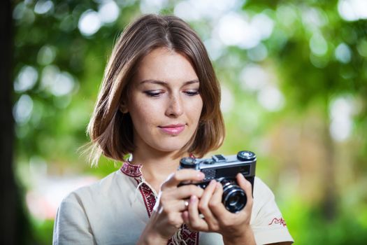 Young woman looking at screen of retro style camera and smiling