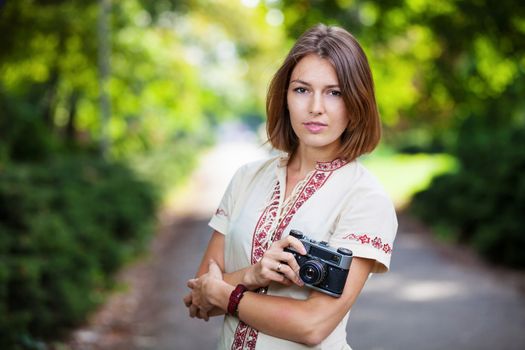 Young attractive woman holding retro style camera in summer park