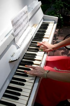 Female hand with red fingernails on the keys of the old white piano
