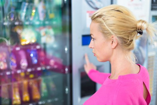 Caucasian woman wearing pink using a modern vending machine. Her right hand is placed on the dia pad.