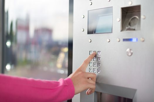 Lady's hand using a dial pad on a vending machine. The fore finger is placed on the dial pad key.