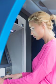 Blonde lady using an automated teller machine . Woman withdrawing money or checking account balance.