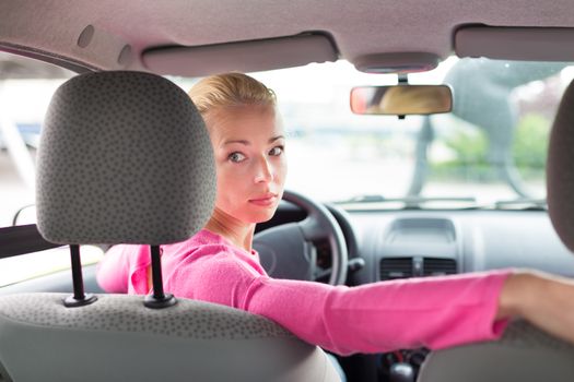 Beautiful young lady looking back through the rear window from the front seat of a car while reversing.