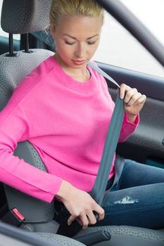 Safety first. Blonde lady fastening her seat belt inside a car. 