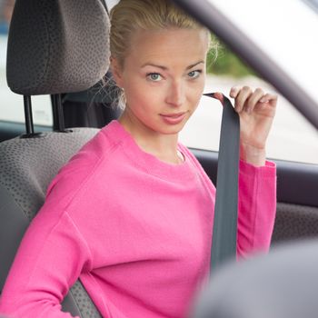 Blonde lady fastening her seat belt inside a car 