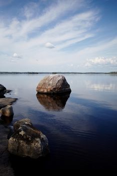 Water landscape with stones. Stones in water. The lake with stones. Beautiful landscape. Water smooth surface and the blue sky with clouds.