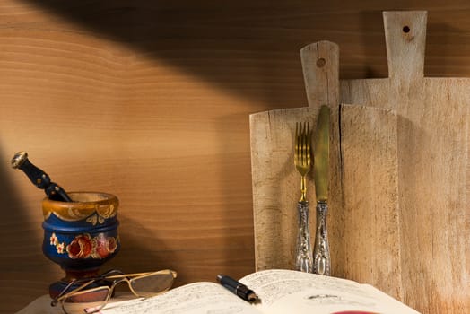 Wooden wall with two cutting boards, old silverware, recipe book, glasses and mortar with pestle. Concept of rustic cuisine