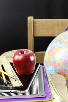 Red apple with school supplies and tablet sitting on an antique school desk.