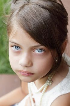 Young girl looking directly into the camera, wearing vintage pearl necklace and hair pulled back. Extreme shallow depth of field with selective focus on eyes.