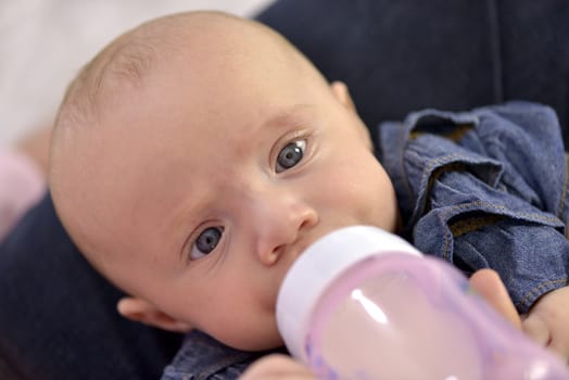 Close-up of a baby girl with beautiful blue eyes bottle feeding

