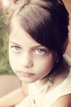 Young girl looking directly into the camera, wearing vintage pearl necklace and hair pulled back. Extreme shallow depth of field with selective focus on eyes.