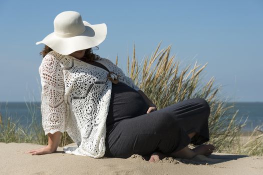 pregnant woman holding her hands on her belly with beach on background