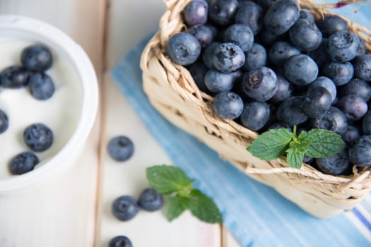 Fresh organic blueberries in basket and pot with yogurth on white background retro kitchen table