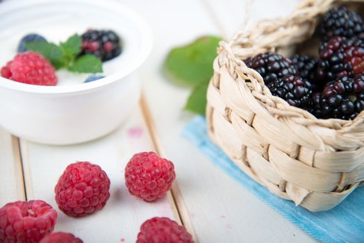 fresh organic berrys fruits in basket and pot of yogurth over blue kitchen cloth on white background retro style wooden table