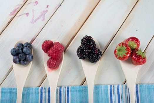 fresh organic berrys fruits on wooden spoon over blue kitchen cloth on white background retro style wooden table