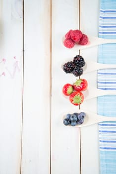 fresh organic berrys fruits on wooden spoon over blue kitchen cloth on white background retro style wooden table