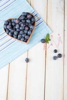 fresh organic blueberries in heart style shape basket and blue kitchen cloth on white background retro kitchen table