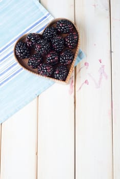 fresh organic blackberries in heart style shape basket  on white background retro kitchen table and blue kitchen cloth