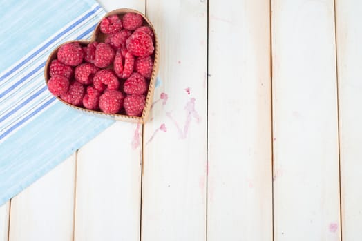 fresh organic raspberries in heart style shape basket  on white background retro kitchen table and blue kitchen cloth