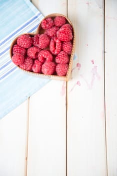 fresh organic raspberries in heart style shape basket  on white background retro kitchen table and blue kitchen cloth