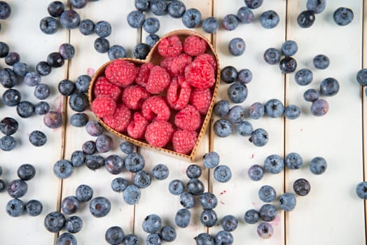 fresh organic raspberries and blueberries in heart style shape basket  on white background retro kitchen table